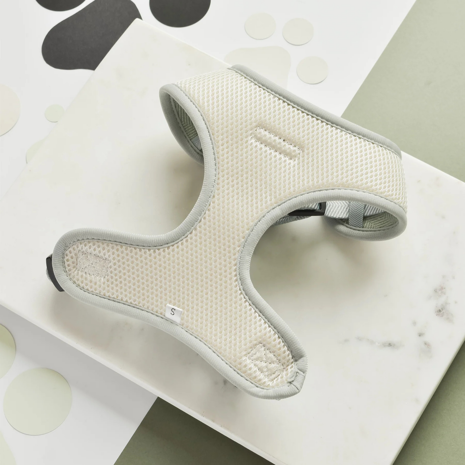 Gray harness on a marble surface with paw prints in the background