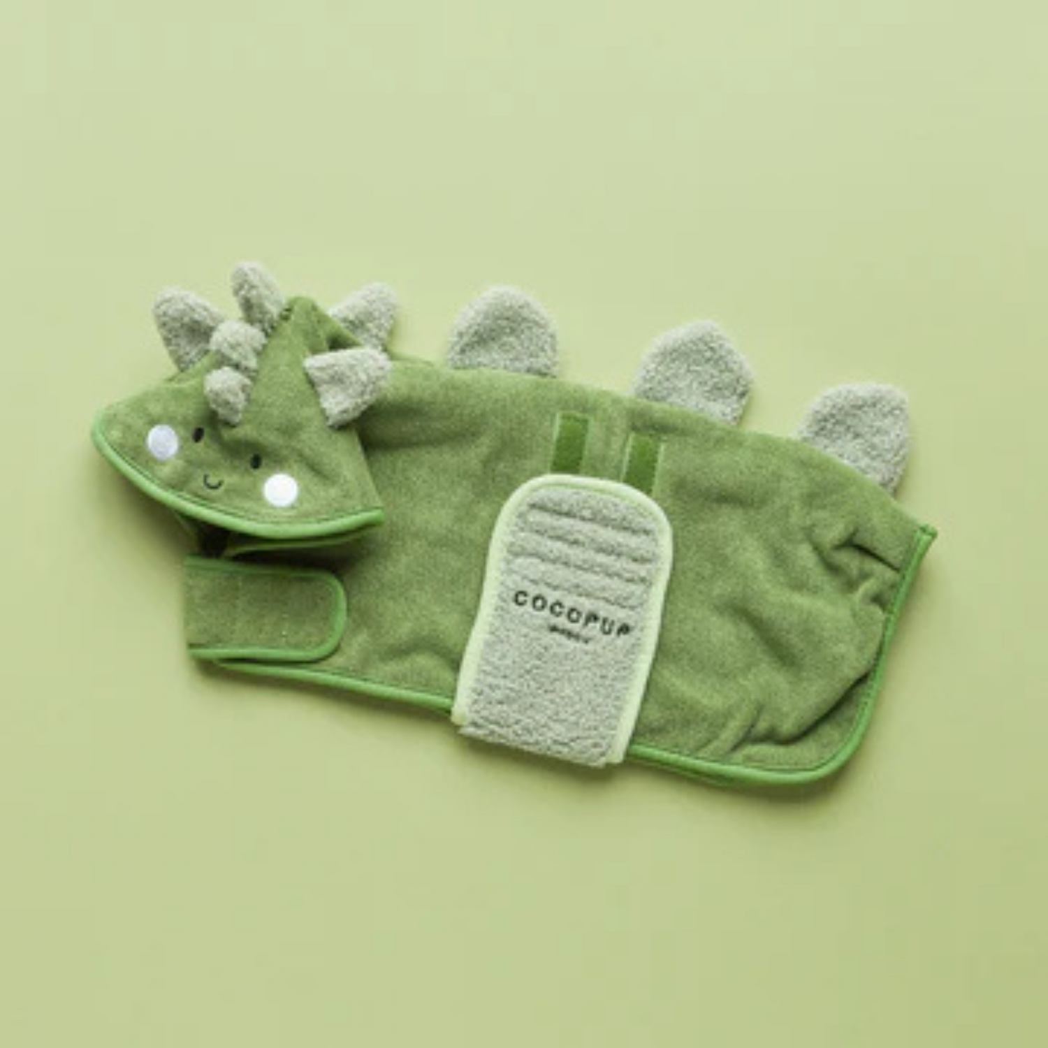Green dinosaur-shaped towel with a small paddle on a light green background