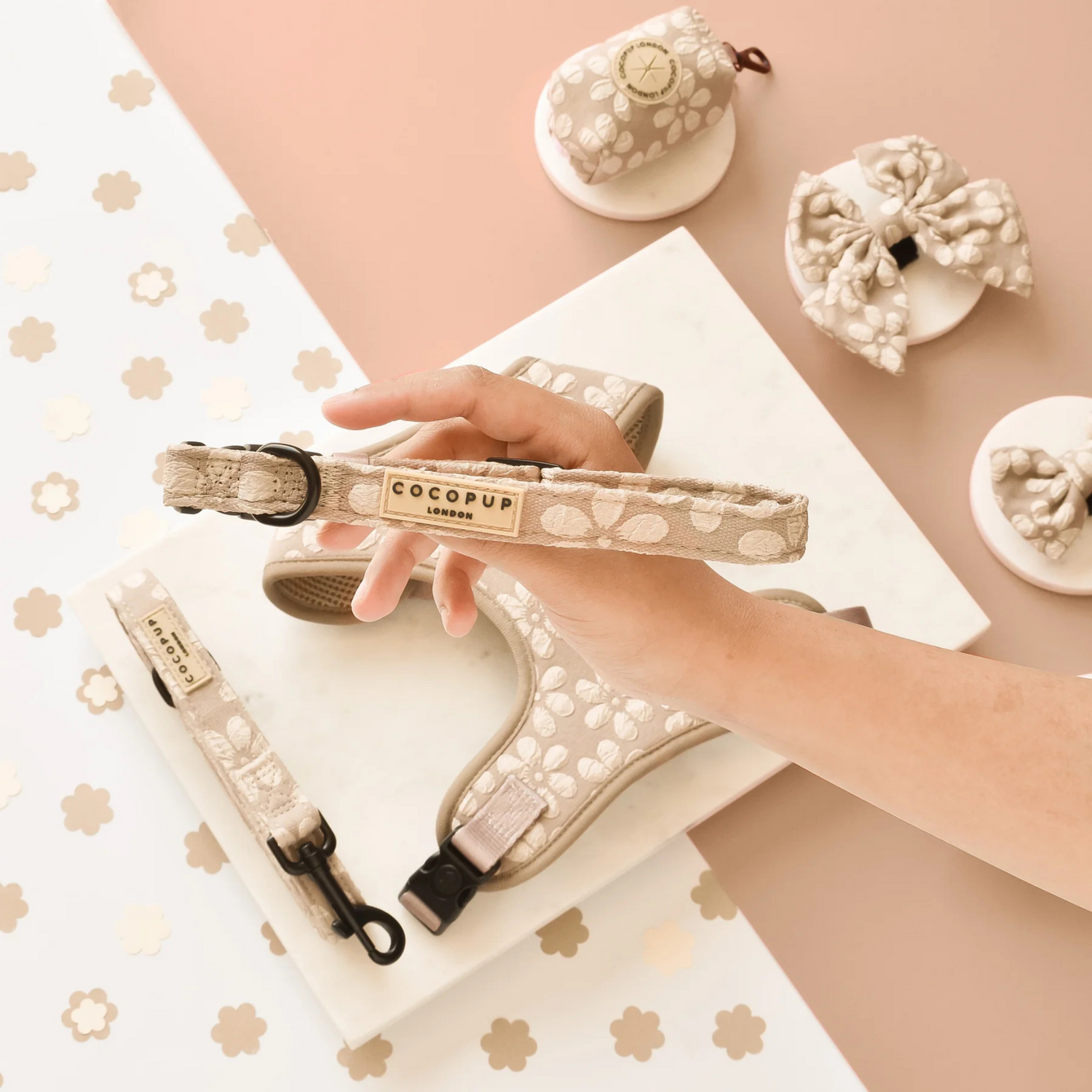 Cocopup dog collar and leash set held by a hand on a decorative background with small white flowers.