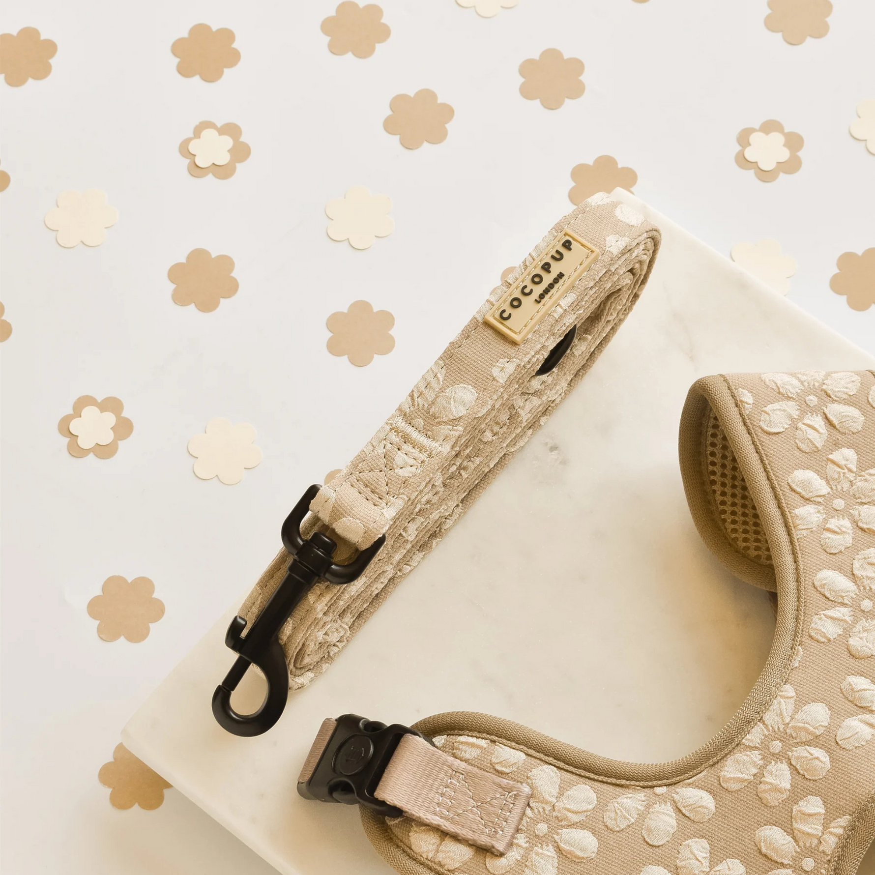 Beige dog harness and leash set on a white surface with a floral patterned background