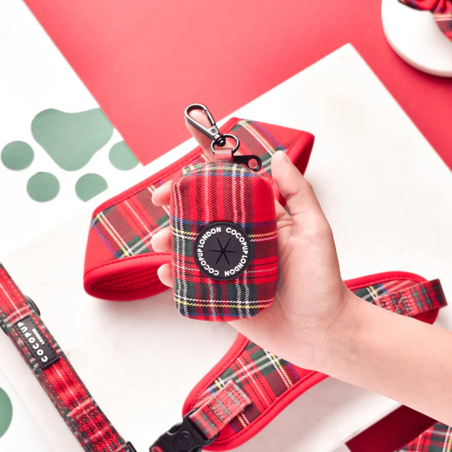 Red plaid pet collar and leash set held by a hand on a red and white background