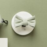 White wall hook with a light green knotted dog bow on a green background