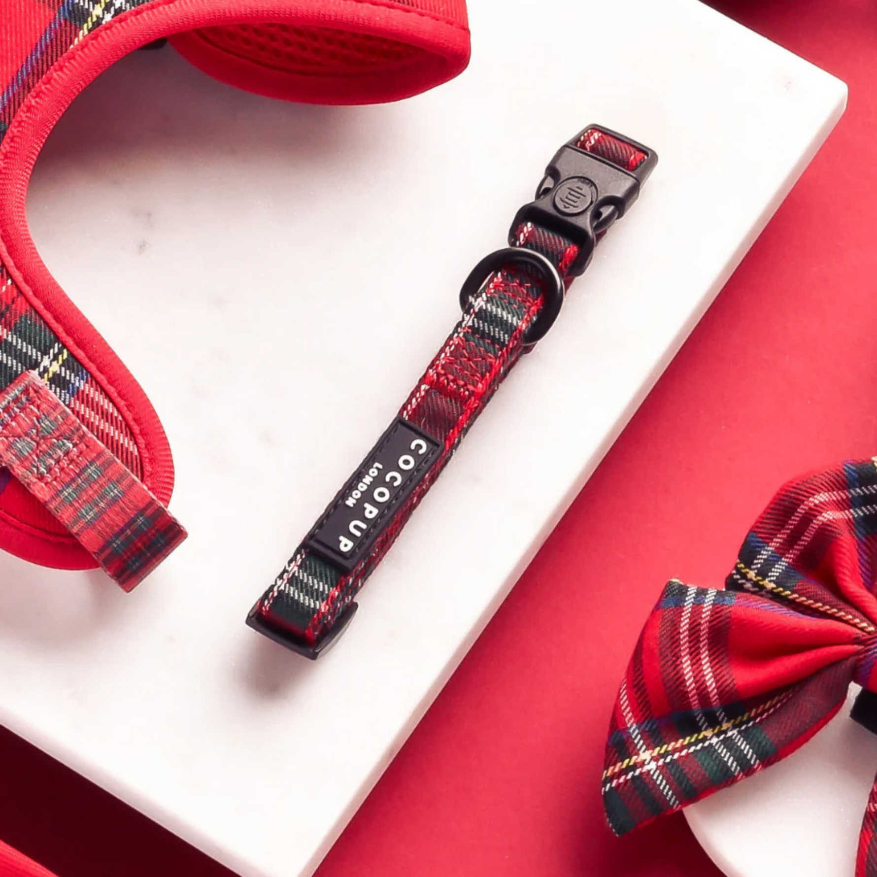Red plaid dog harness, collar, and bow tie set on a red background