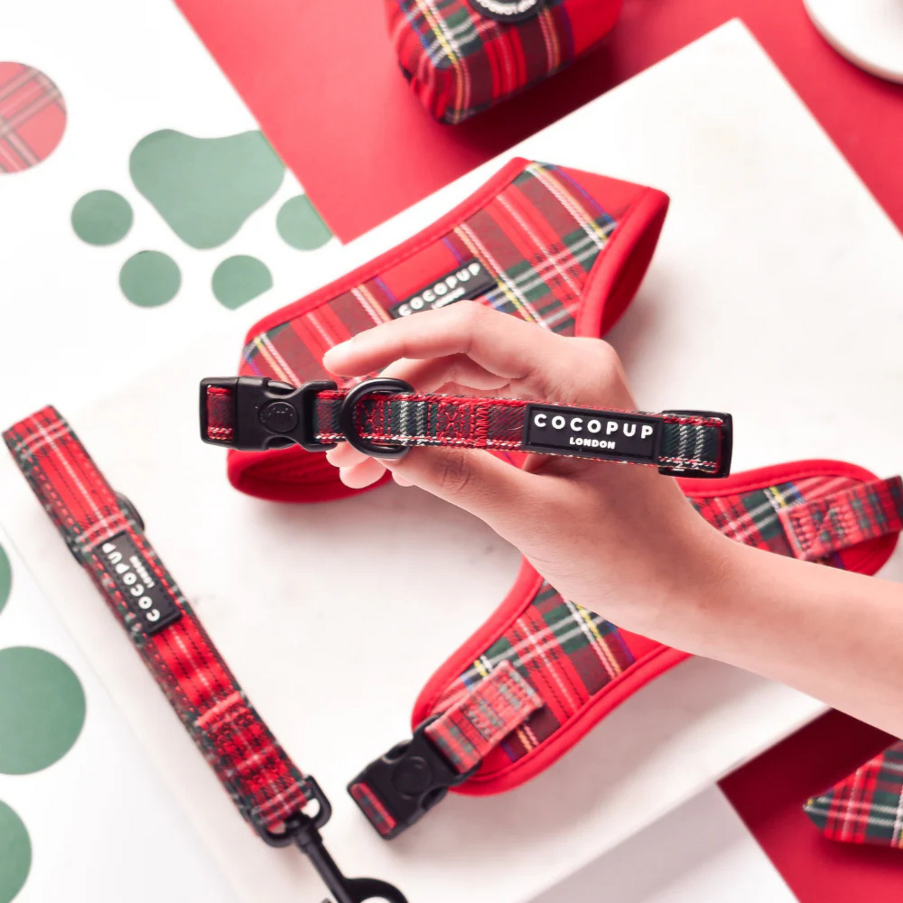 Red plaid dog collar and leash with 'Cocopup' branding held by a hand on a white background.