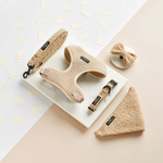 Set of beige pet accessories including a harness, leash, and collar on a light background.