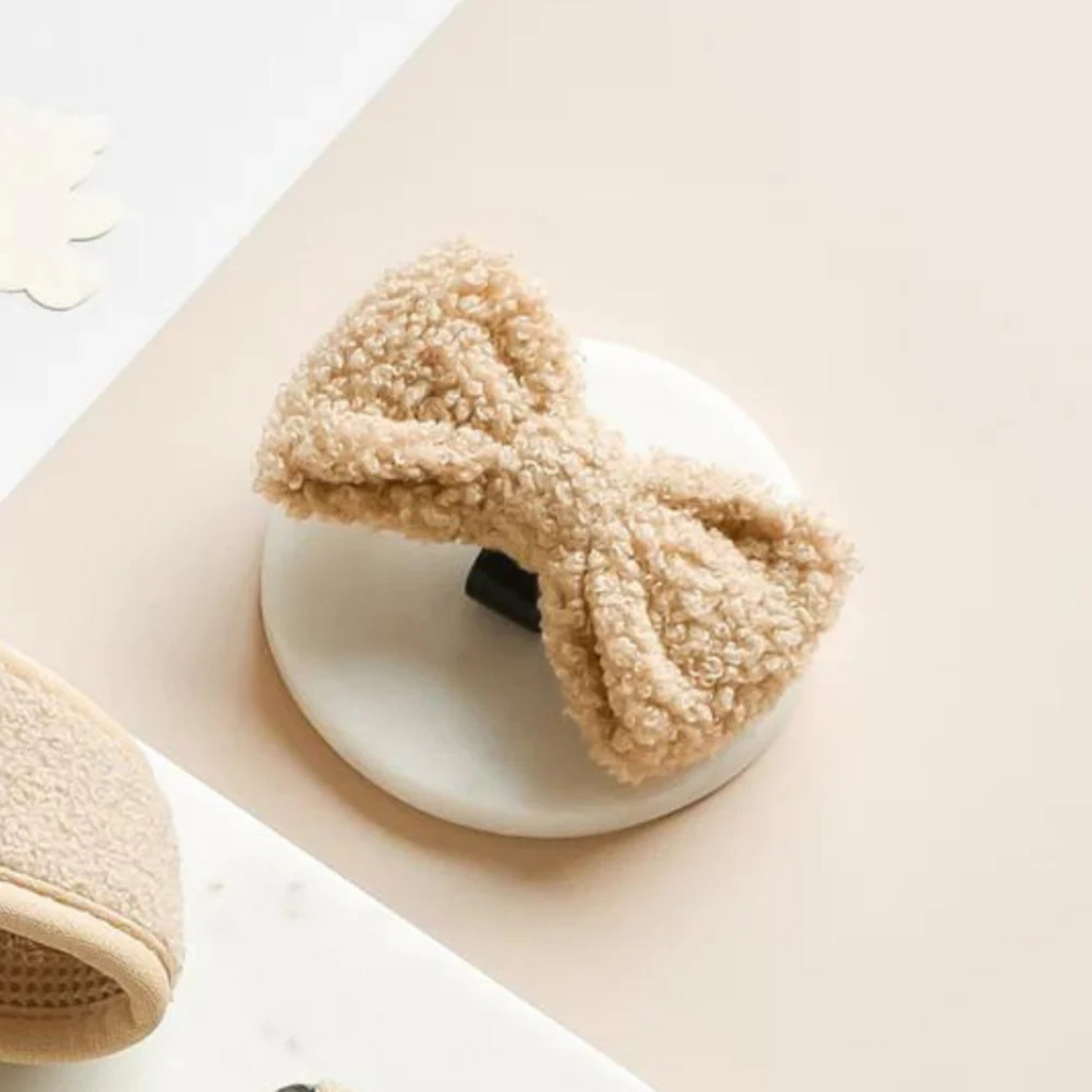 Beige dog bow tie hair accessory on a white plate with a beige background