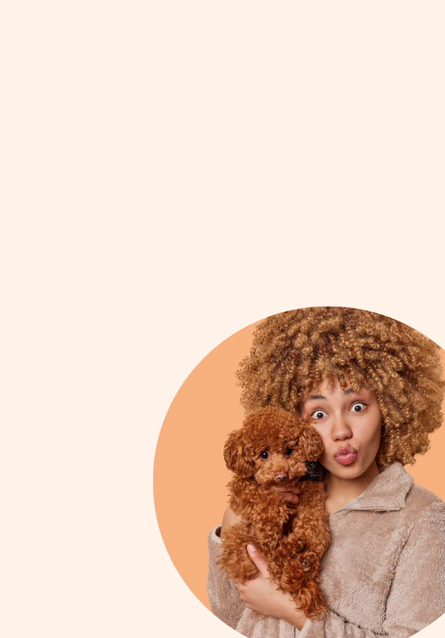 Woman holding a small brown cavoodle dog with a surprised expression on a beige background