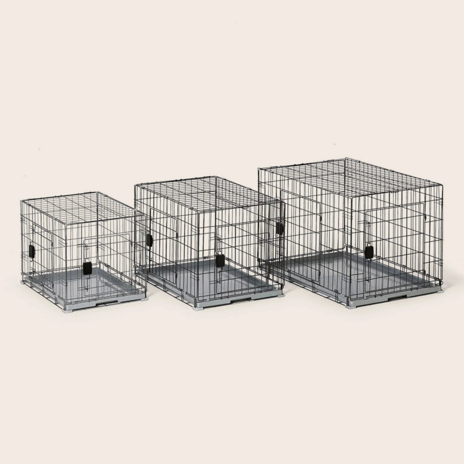 Three black metal pet crates of different sizes on a beige background