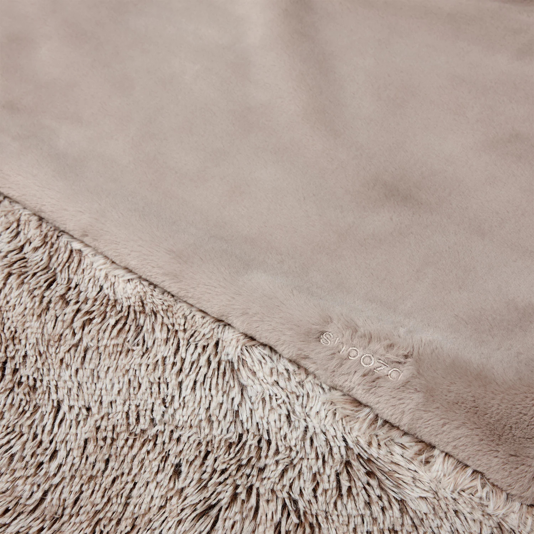 Close-up of a beige blanket with textured edge and brand logo.