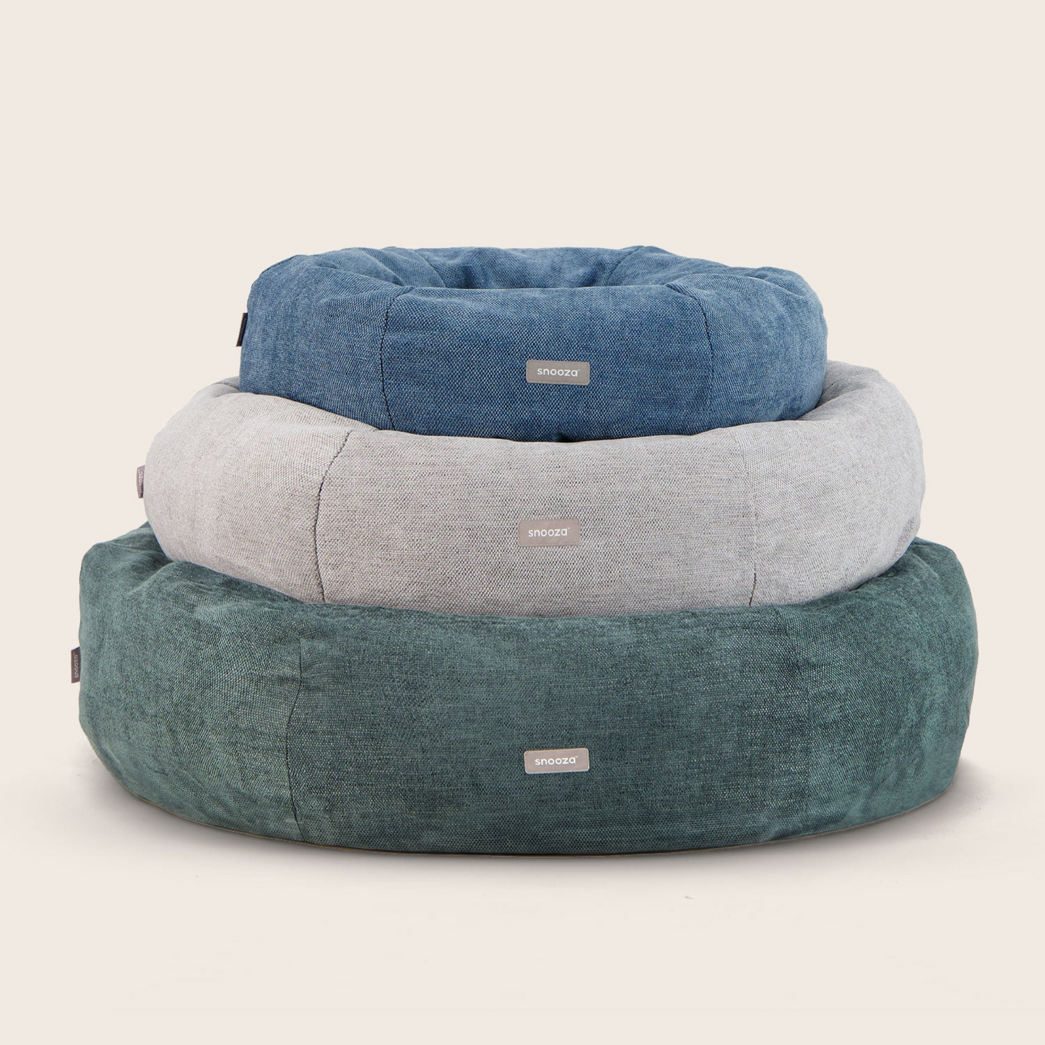 Stack of three dog beds in blue, gray, and green on a beige background