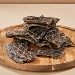 Dried beef jerky pieces on a wooden board with a beige background