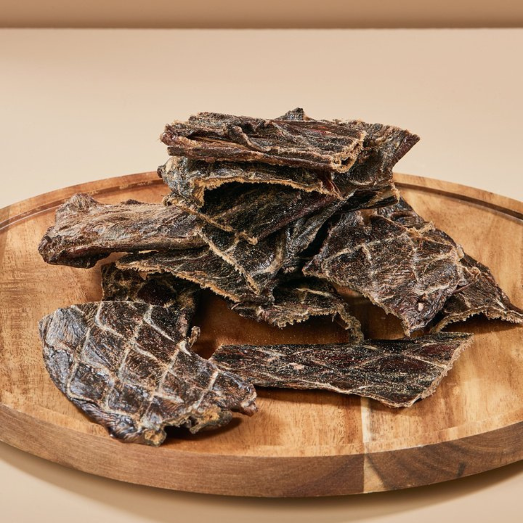 Dried beef jerky pieces on a wooden board with a beige background